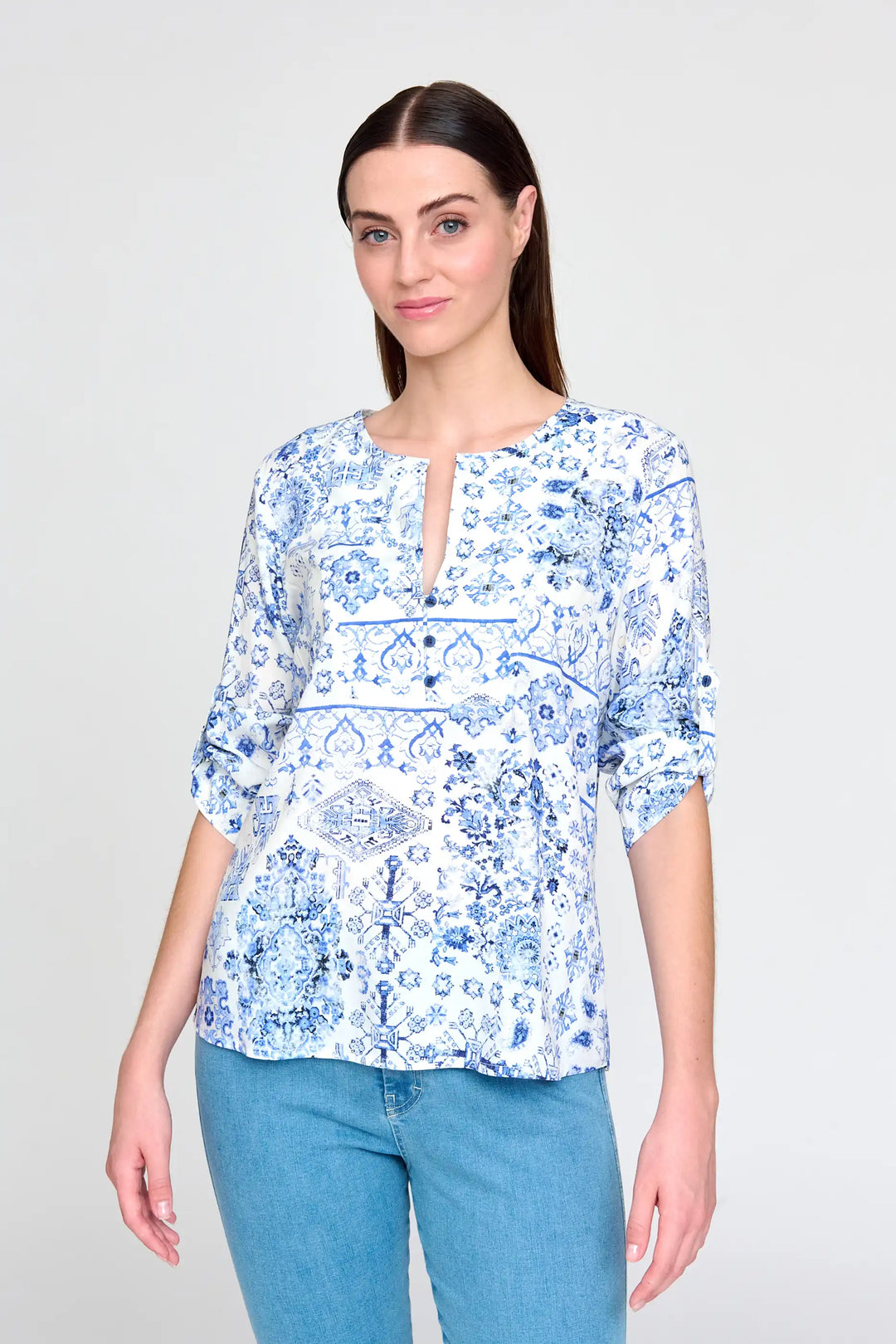 Model showcases 'Acra' style blouse featuring blue and white porcelain print, 3/4 sleeves, and keyhole neckline, complemented by casual light blue jeans.