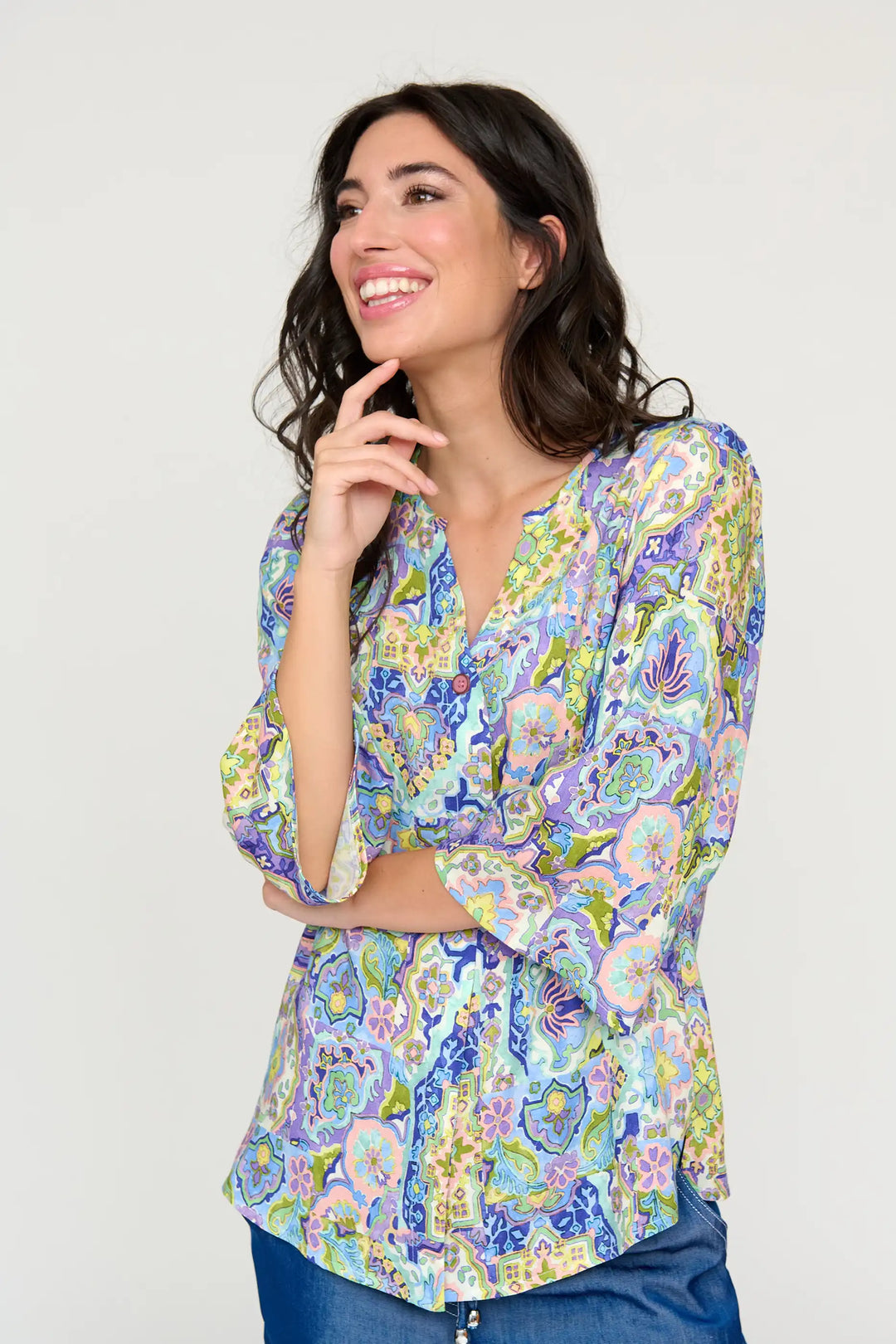 Joyful model wearing the 'Alicia' style blouse with a pastel paisley and floral print, long sleeves, and V-neck, paired with blue denim jeans.