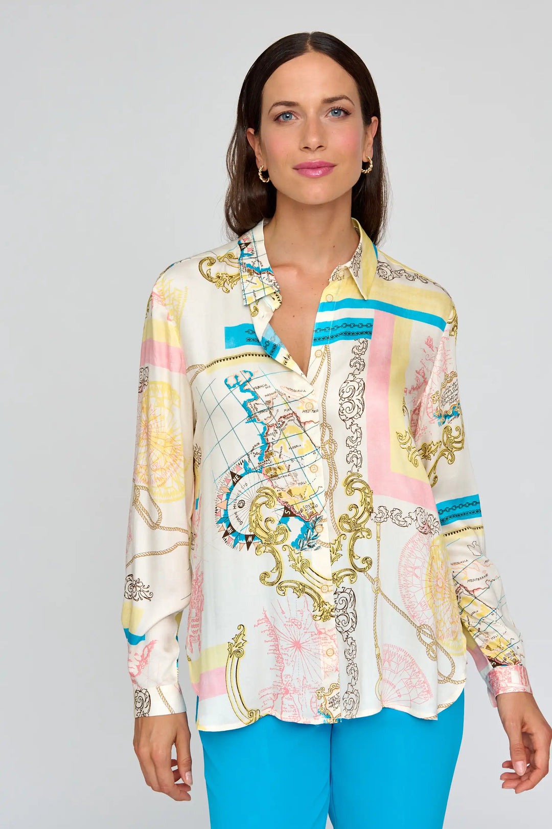Confident model posing in the 'Berrocal' style blouse with nautical and baroque print in pastel colors, full-length sleeves, and a collar, paired with bright blue trousers.