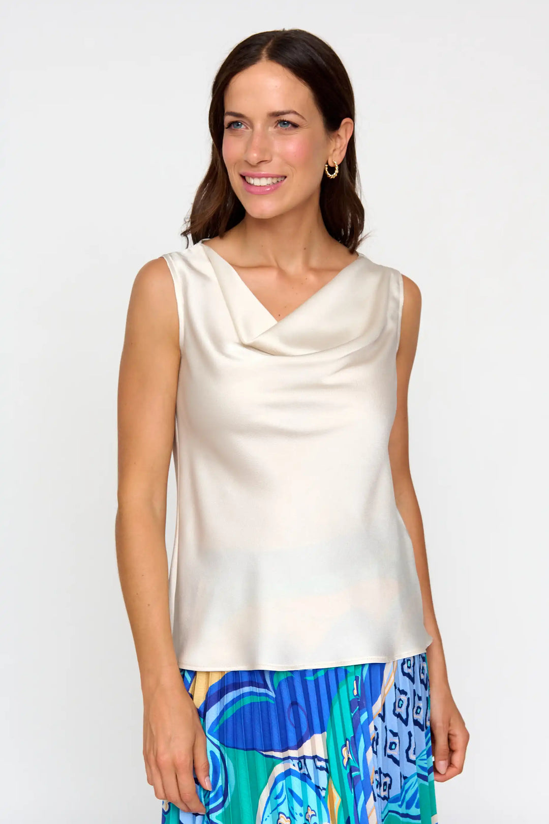 Smiling model in the 'Jerez' style ivory blouse with a soft cowl neckline, sleeveless cut, paired with a vibrant, multi-coloured skirt.