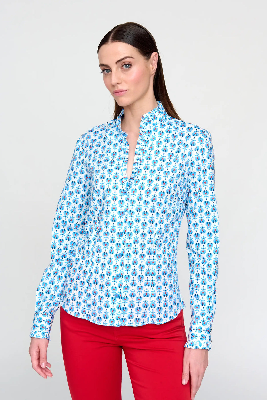A model wearing the 'Luque' style blouse, adorned with a blue floral print, long sleeves, and a V-neck, complemented by red trousers.