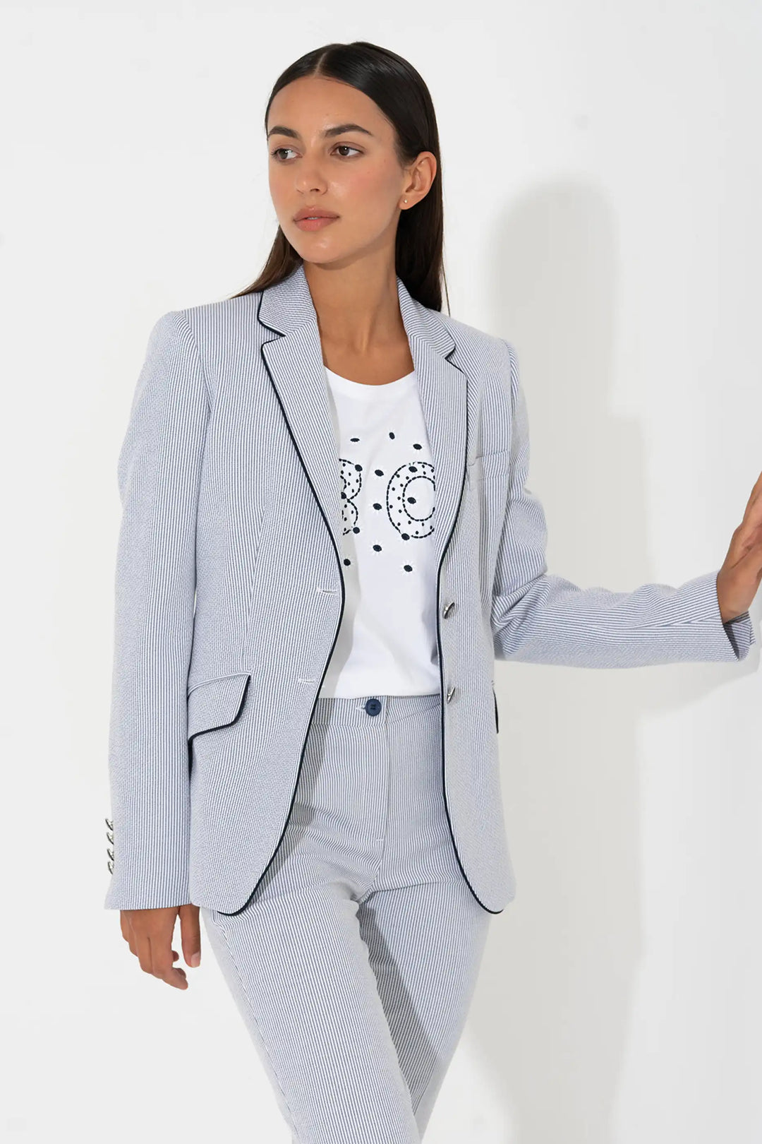 Model in the 'Muralla24' style light blue grey pinstripe blazer with notched lapels and a double-button closure, paired with a casual white tee and coordinating trousers.