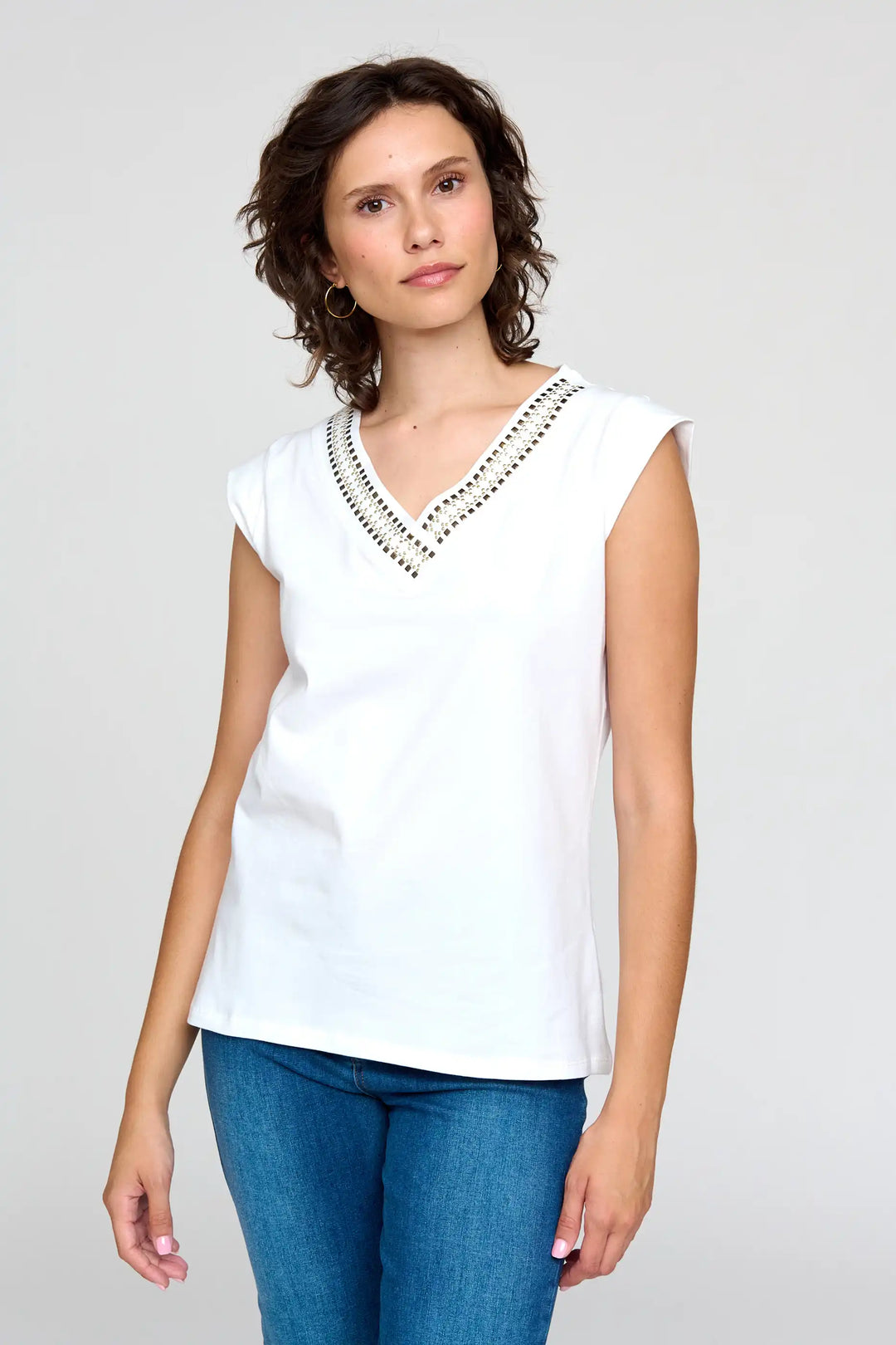 Model wearing the 'Nagoya' style white sleeveless blouse with a studded V-neckline, paired with classic blue jeans.
