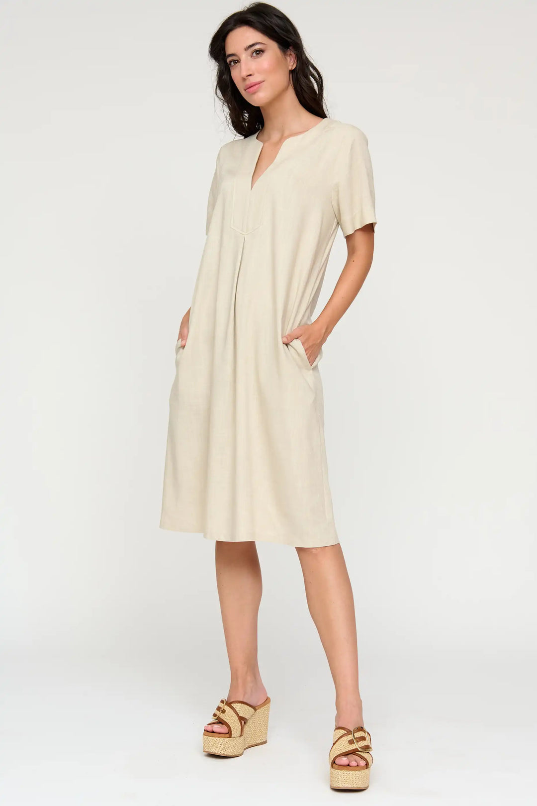 Model in the 'Nieves' style midi dress in a soft neutral tone, with a V-neck, short sleeves, and relaxed fit, paired with textured wedge sandals.