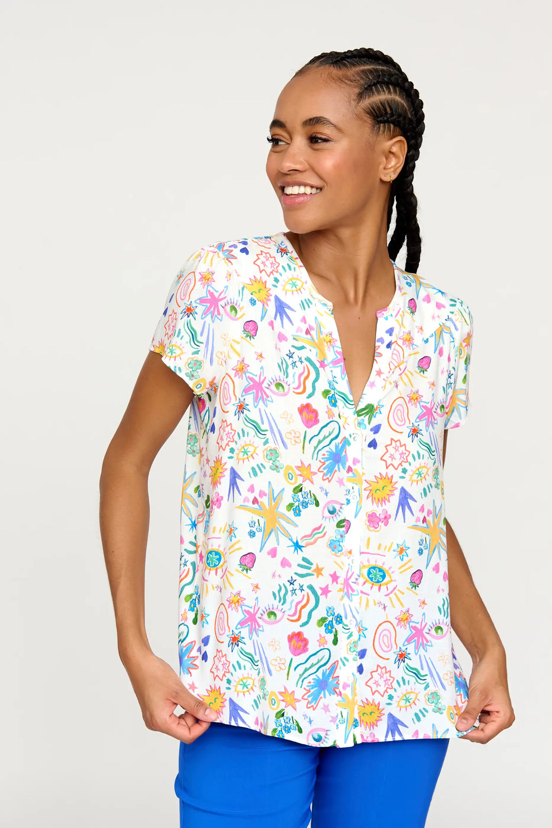 A cheerful model wearing the 'Zali24' style top, adorned with a colourful, playful print of flowers and celestial doodles, featuring a V-neckline and cap sleeves against a light backdrop.