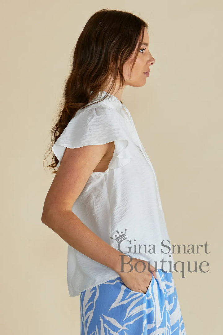 Betty Basics Lyra Blouse side view is a white flutter sleeve blouse with a tie front neckline available at Gina Smart Boutique