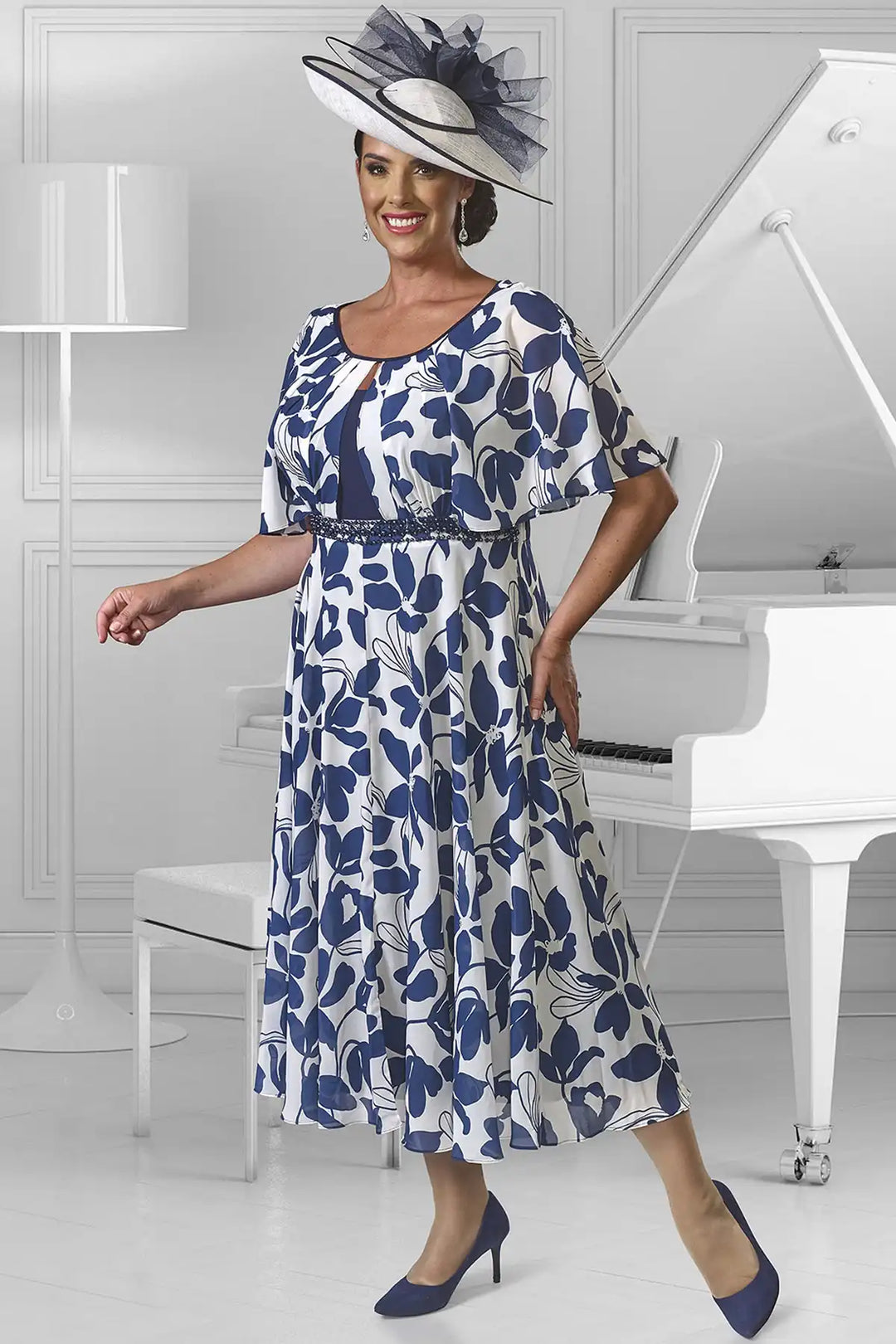 Woman wearing a Dressed Up by Veromia DU582 ivory dress with a navy floral print, featuring a scoop neckline, short sleeves, a navy waistband with shimmering navy beads, and a flowing pleated midi skirt.