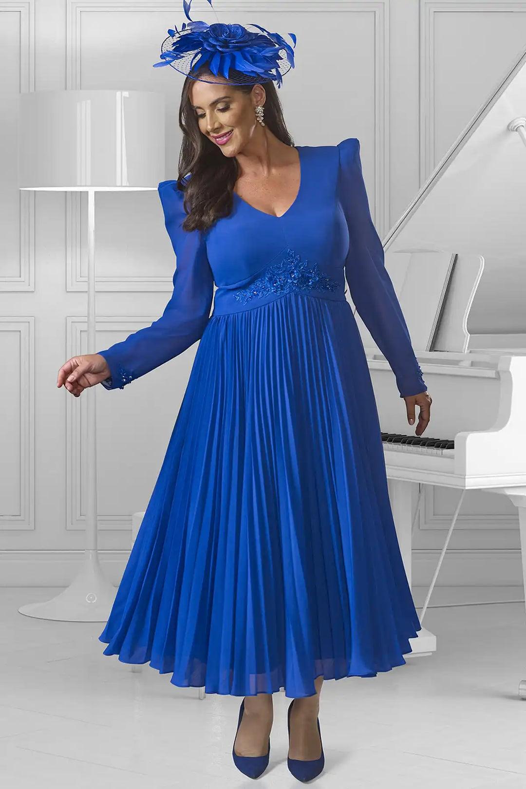 Elegant woman in a Dressed Up by Veromia DU595E full-length pleated cobalt blue gown with V-neckline, long sheer sleeves, and delicate floral lace appliques.