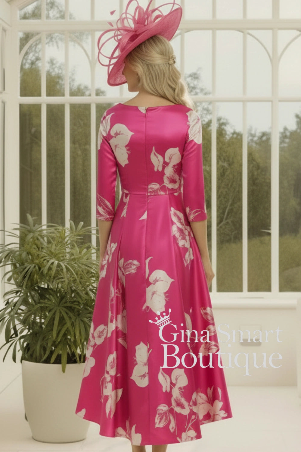 Woman wearing a pink floral dress and hat in front of a white railing.