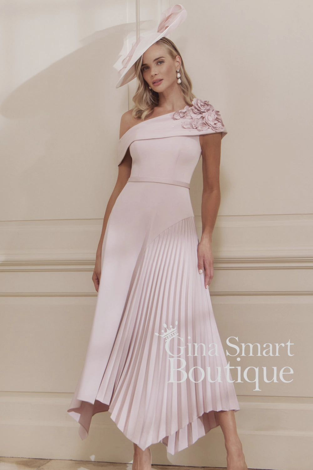 John Charles petal pink one-shoulder dress with 3D floral corsage, sunray pleated skirt, and matching hat – romantic Mother of the Bride outfit.