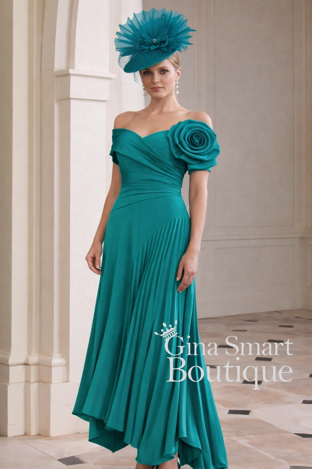 John Charles peacock teal off-the-shoulder dress with statement 3D rose shoulder, pleated skirt, and matching hat – dramatic Mother of the Bride outfit.