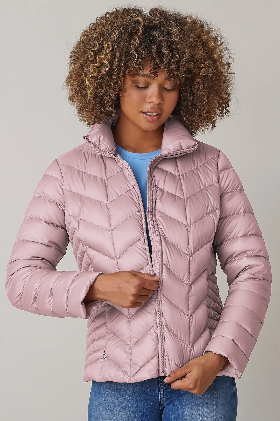Model wearing a pale pink quilted jacket with a high collar and zipper, styled over a blue top and denim jeans, style 0124-2040-62-33