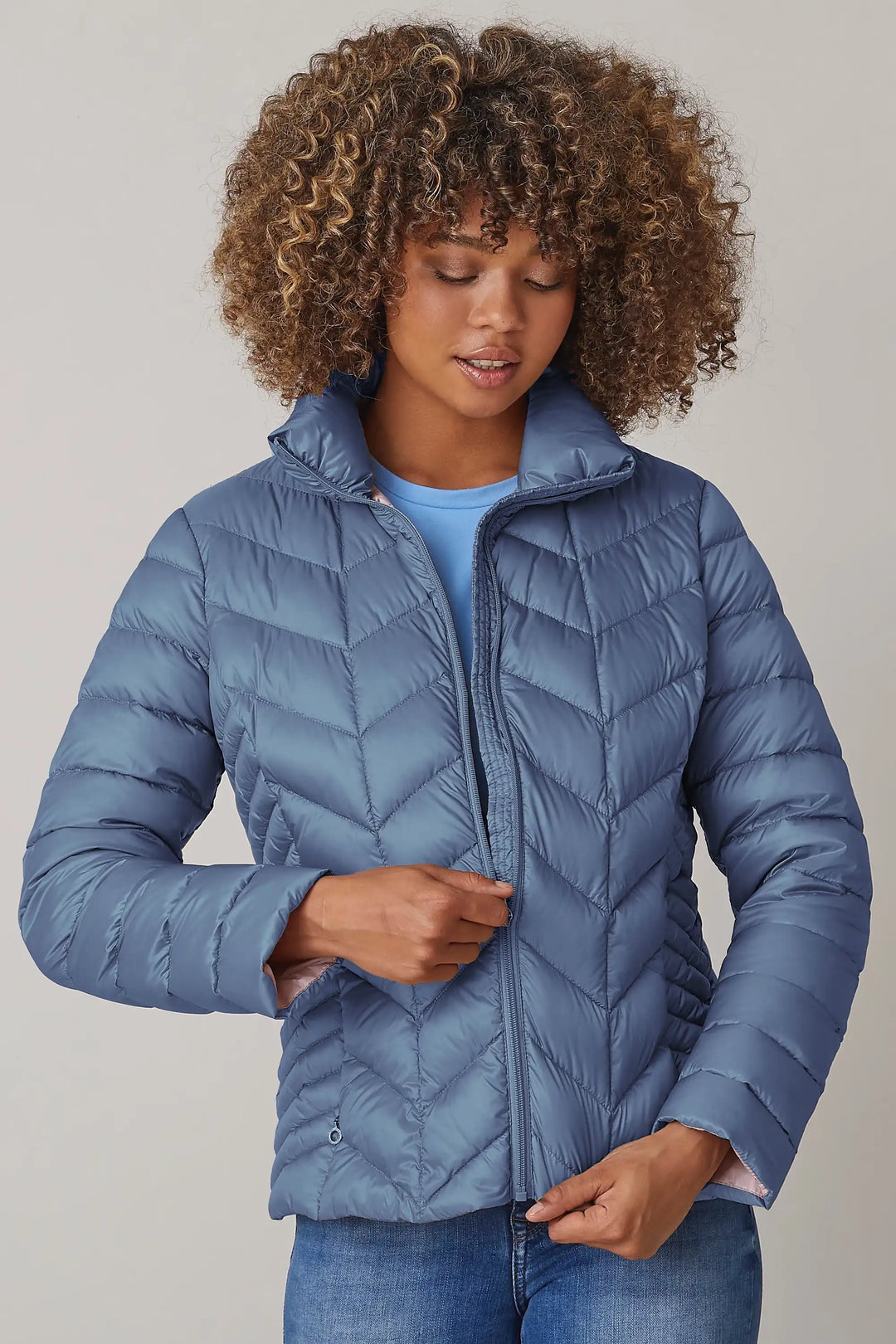 Woman wearing a slate blue quilted jacket with a high neckline and zip front, over a light blue shirt, paired with denim jeans, style 0124-2040-62-55