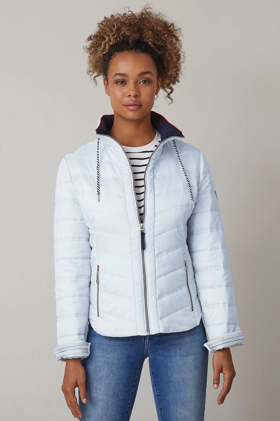 Model with curly hair wears a light blue quilted jacket with a front zipper, striped lining, and contrasting navy and red details on collar and cuffs, paired with a striped shirt and jeans, style 0124-2454-66-51